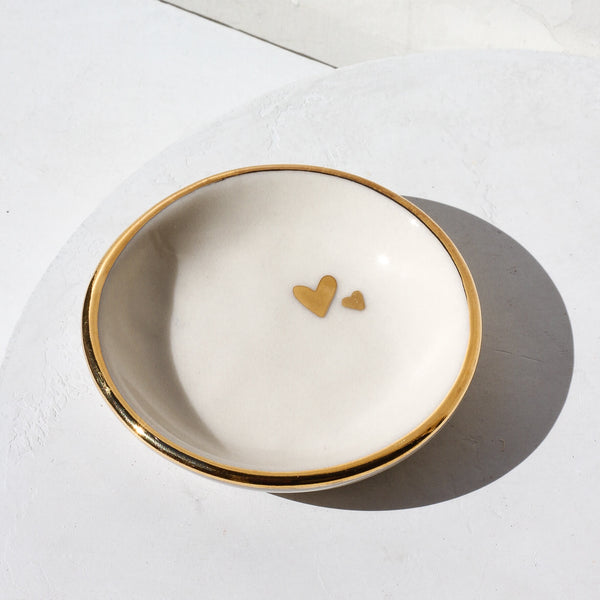 A gilded white trinket dish with 2 gold hearts in the top right of the dish.